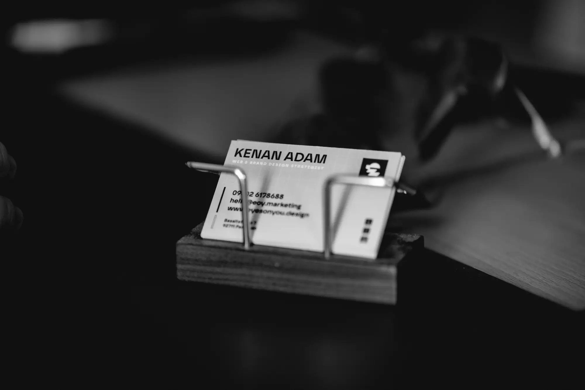 Visitenkarte von Kenan Adam im Holzhalter auf dem Schreibtisch