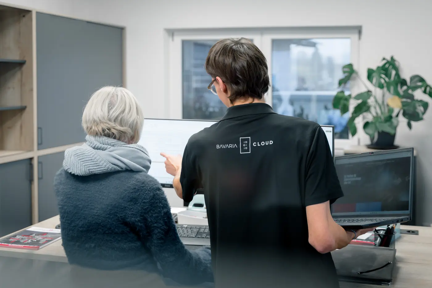 Junger IT-Mitarbeiter von BavariaCloud hilft einer Kundin am Arbeitsplatz