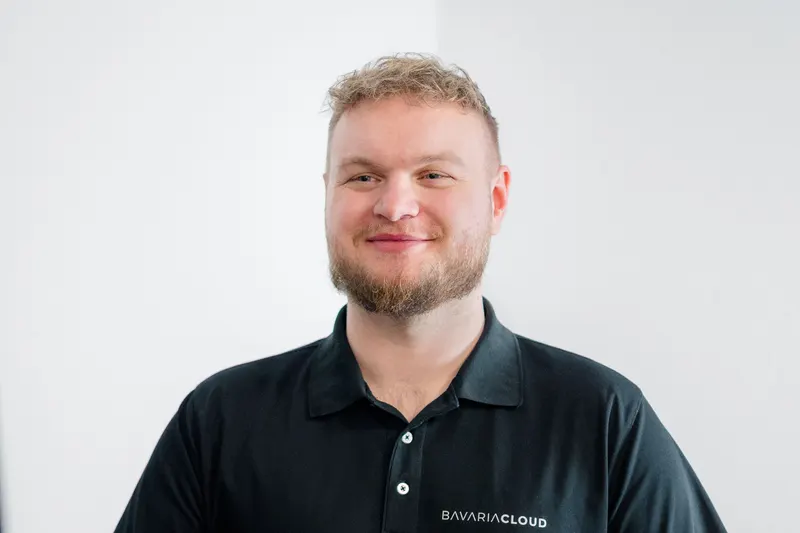 Mitarbeiter von BavariaCloud im Poloshirt lächelt an seinem Arbeitsplatz, die Hände auf der Tastatur