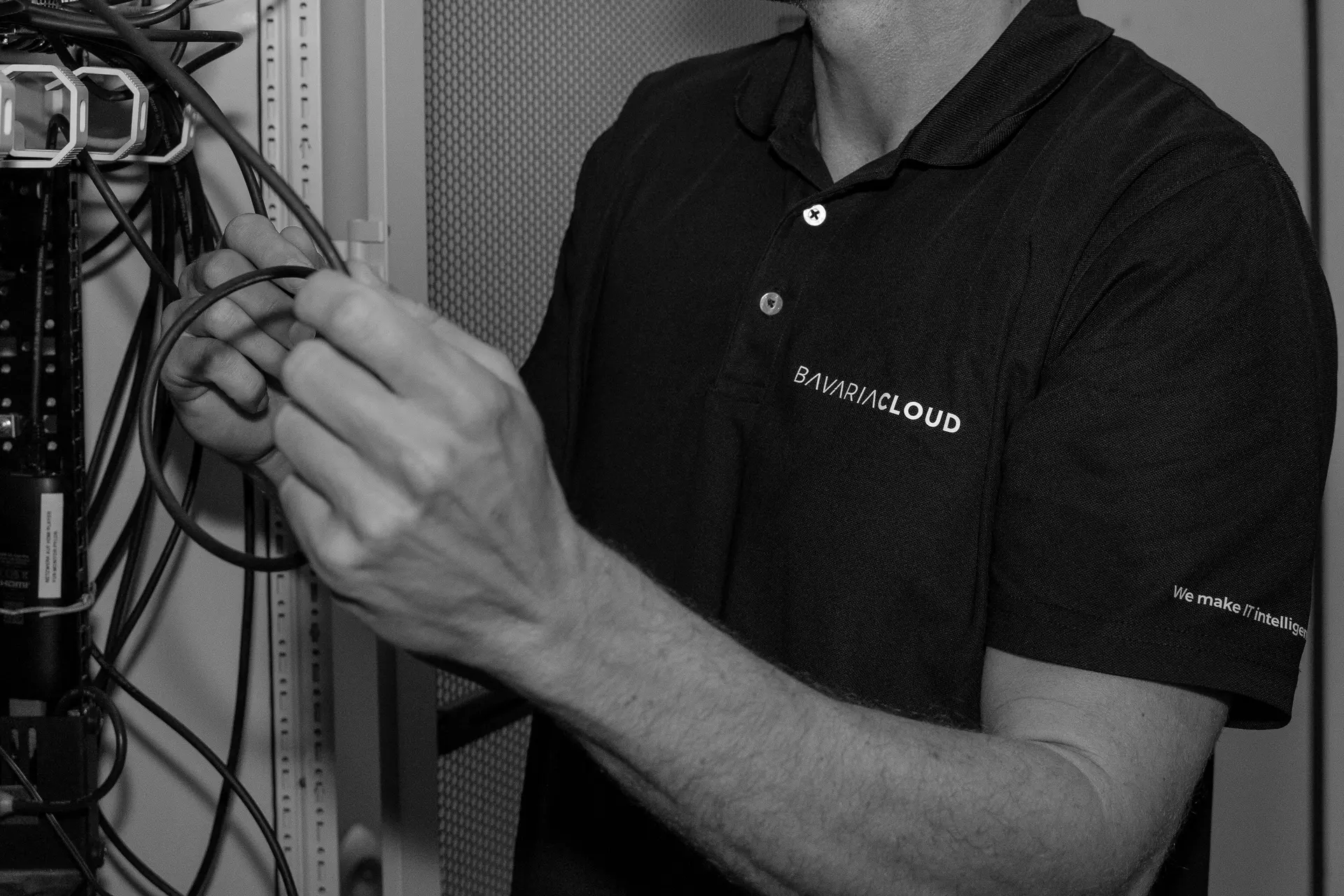 Hände eines BavariaCloud-Technikers an der Verkabelung eines Netzwerkschranks, schwarzweiß