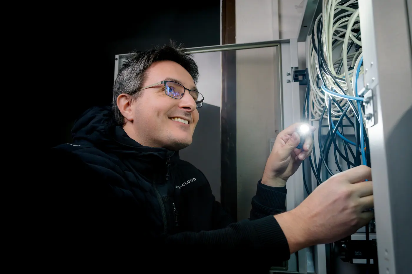 Lächelnder Techniker von BavariaCloud prüft die Verkabelung in einem Netzwerkschrank