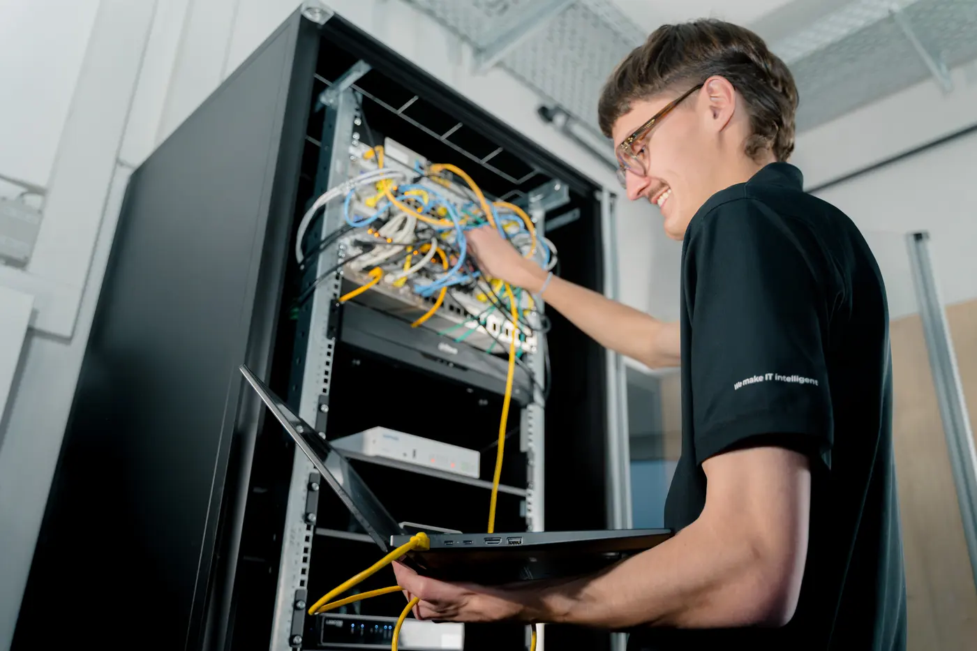Junger Techniker von BavariaCloud arbeitet mit Laptop an einem offenen Serverschrank