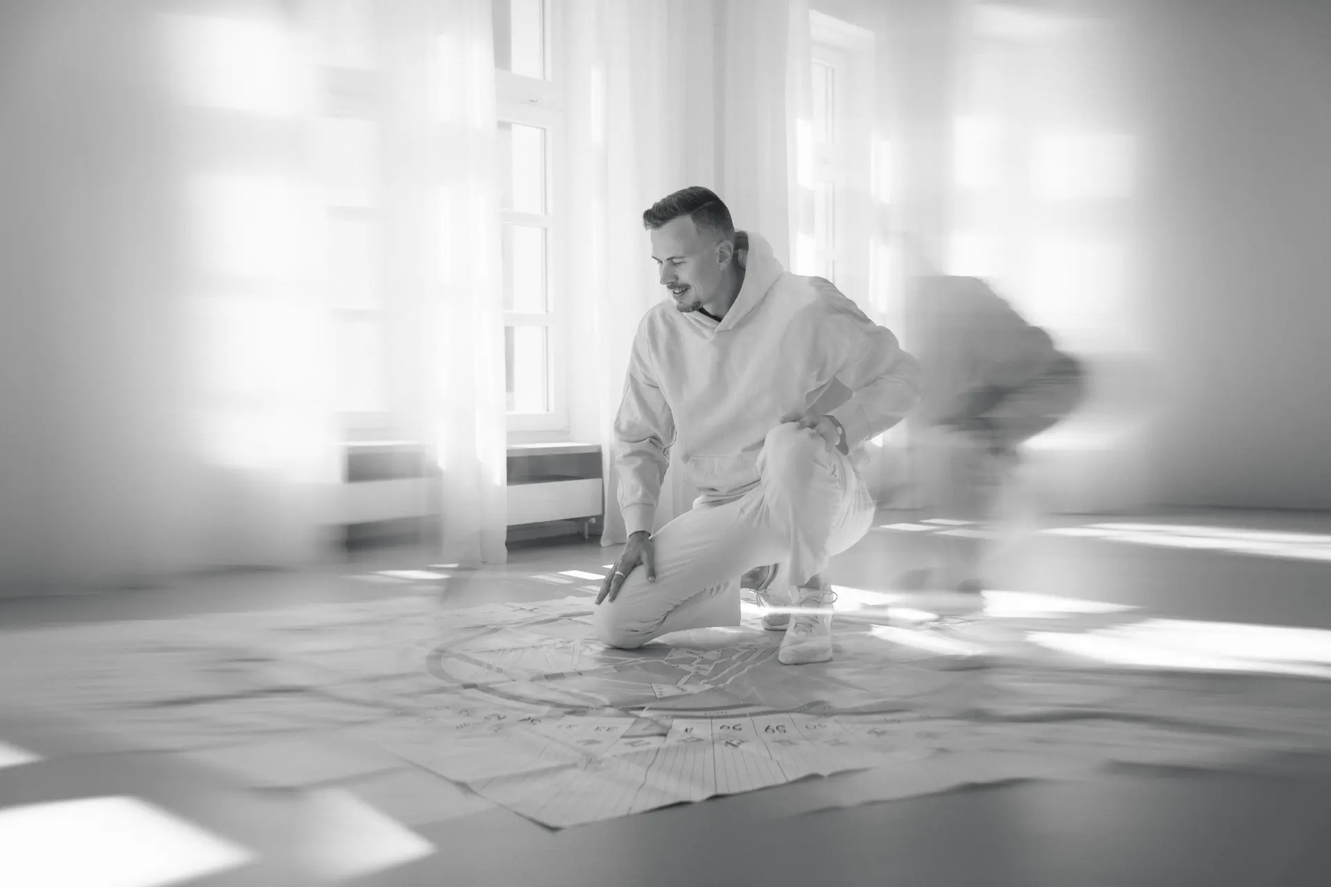 Daniel Bayer kniet in einem hellen Raum über ausgebreiteten Blättern mit einem Human-Design-Chart