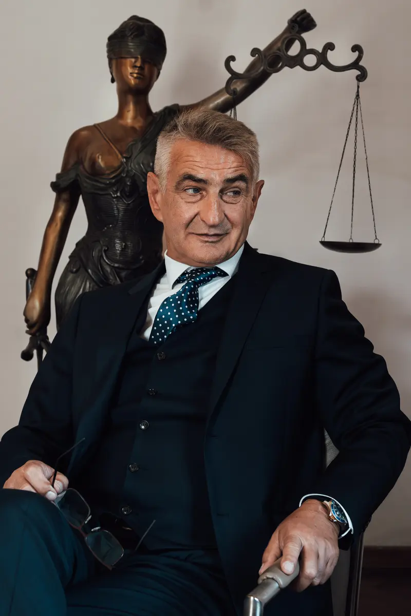 Helmut Mörtl sitzt vor einer Justitia-Statue mit Waage