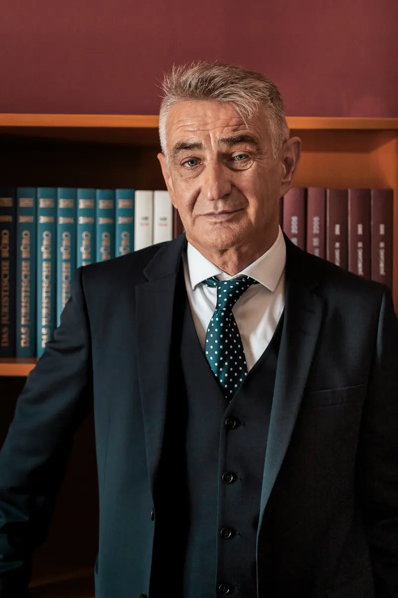 Helmut Mörtl im dunklen Anzug vor einem Bücherregal mit Gesetzbüchern