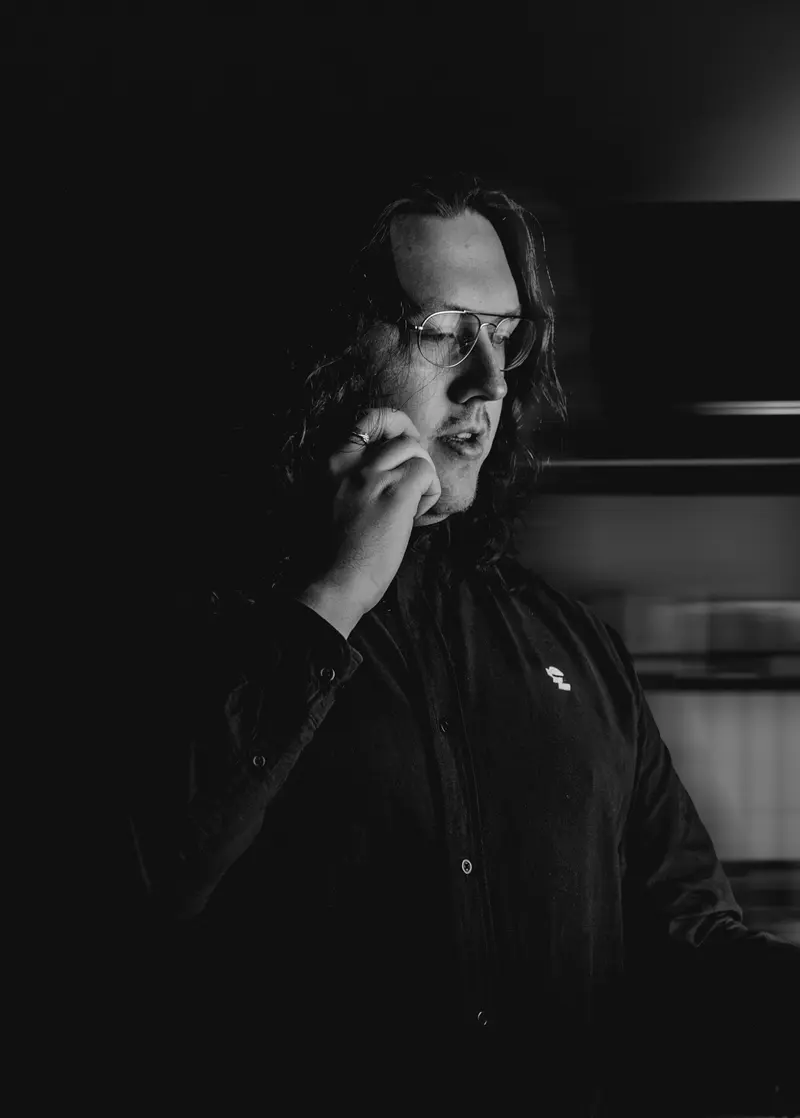 Kenan Adam, Inhaber von eyes on you, im dunklen Hemd, nachdenklich mit der Hand am Kinn, schwarzweiß
