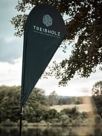 Instagram-Beitrag: Beachflag der Treibholz Beachbar vor Bäumen am See