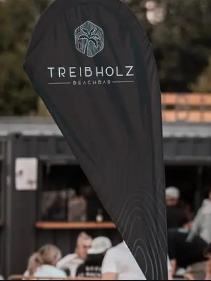 Instagram-Beitrag: Beachflag vor der Bar, dahinter Gäste