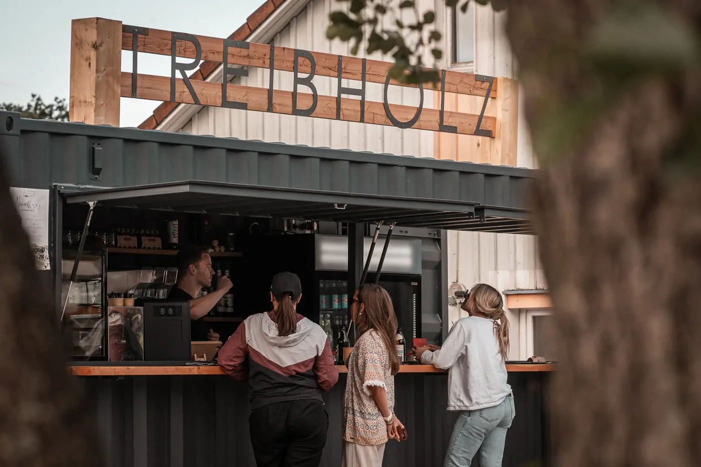 Gäste an der Theke der Treibholz Beachbar unter dem großen Holzschriftzug