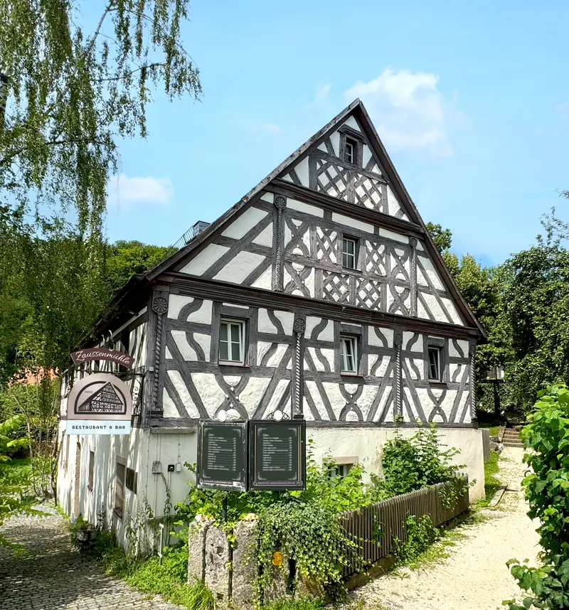 Die Zaussenmühle heute: Fachwerkhaus mit Giebel, Biergarten und Hauslogo am Eingang